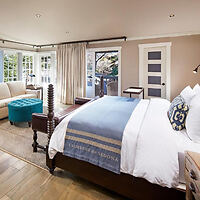 Elegantly designed bedroom with a king-sized bed, blue-striped comforter, and French doors opening to a sunny outdoor area